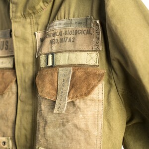 May include: A green military jacket with multiple pockets and straps. The jacket has a patch that reads "NW CHEMICAL-BIOLOGICAL, FIELD, MI7A2".