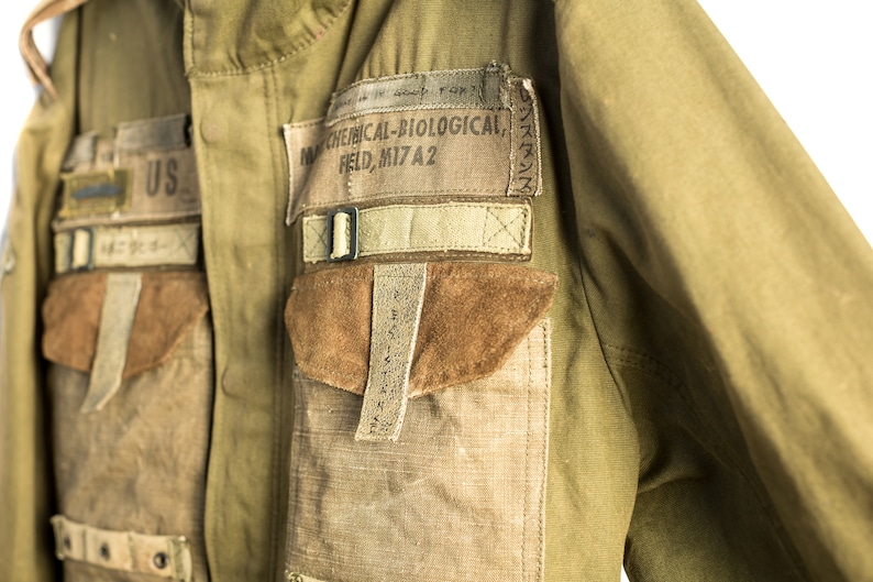May include: A green military jacket with multiple pockets and straps. The jacket has a patch that reads "NW CHEMICAL-BIOLOGICAL, FIELD, MI7A2".