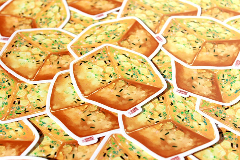 May include: A collection of stickers featuring a square-shaped illustration of a piece of garlic bread. The bread is golden brown with green and black flecks, and a white border. The stickers are scattered across the image.
