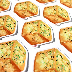 May include: A collection of stickers featuring a detailed illustration of a piece of garlic bread. The bread is golden brown with green and black toppings, set against a white background.