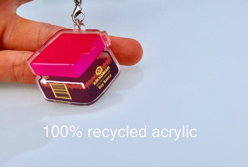 May include: A pink and clear acrylic keychain shaped like a bottle of Kikkoman soy sauce. The keychain is made from 100% recycled acrylic.