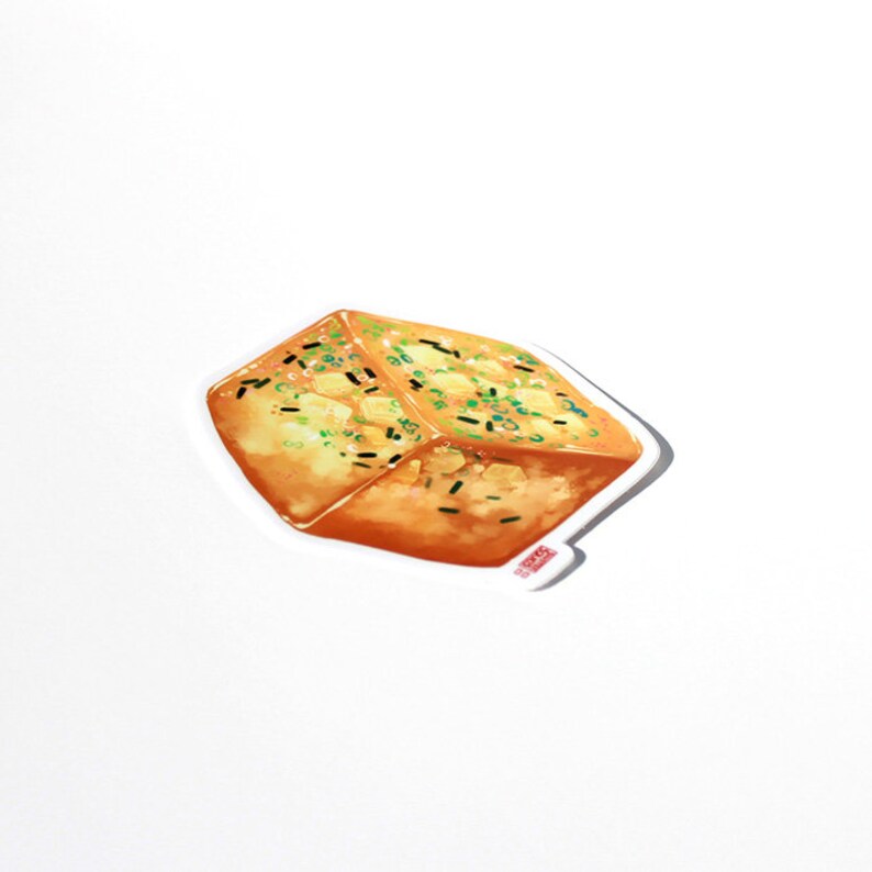 May include: A sticker featuring a watercolor illustration of a piece of fried tofu, garnished with green onions and black sesame seeds. The tofu is golden brown with a slightly crispy appearance, and the sticker has a white border.