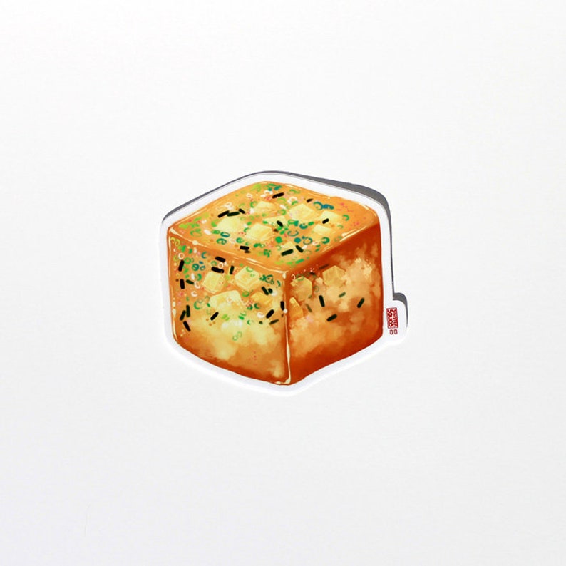 May include: A sticker featuring a square of golden-brown food, possibly tofu or a similar dish. It is garnished with green onions and black sesame seeds. The sticker has a white border and a small logo in the bottom right corner.