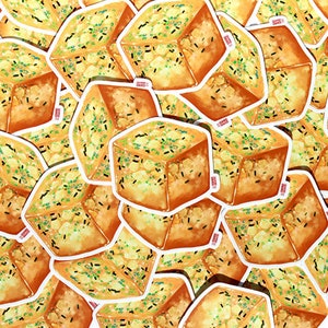 May include: A collection of stickers featuring a watercolor illustration of a cube-shaped food item. The food has a golden-brown exterior, a light yellow interior, and is sprinkled with green and black specks. The stickers have a white border.