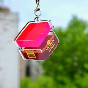 May include: A pink and brown acrylic keychain shaped like a bottle of Kikkoman soy sauce. The keychain has a silver metal ring.