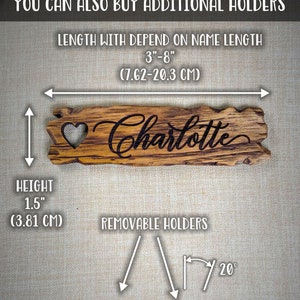 Op de afbeelding: Een houten bord met de naam "Charlotte" erop gegraveerd. Het bord is 3,81 cm hoog en 7,62 tot 20,3 cm lang. Het wordt geleverd met afneembare houten houders die kunnen worden gebruikt om het bord op een plank of tafel te plaatsen. De houders zijn in een hoek van 20 graden geplaatst.