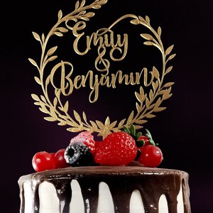 May include: A white cake with chocolate frosting and fresh berries, topped with a gold cake topper that reads "Emily & Benjamin" in cursive.