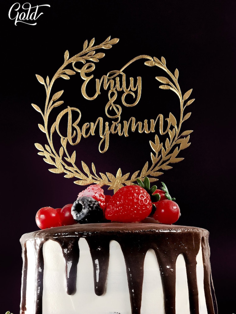 May include: A white cake with chocolate frosting and fresh berries, topped with a gold cake topper that reads "Emily & Benjamin" in cursive.