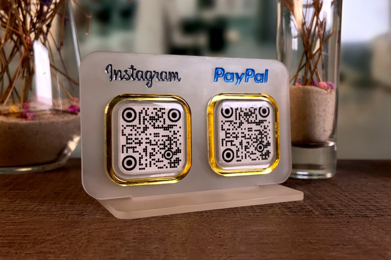 May include: A white acrylic stand with two gold-rimmed square QR code stickers. The left sticker has "Instagram" printed above it and the right sticker has "PayPal" printed above it.