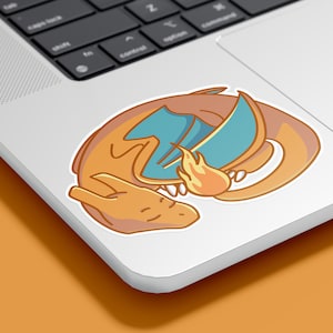 May include: A cartoon illustration of a curled up orange and blue dragon with a flame coming out of its mouth. The dragon is sleeping on a white laptop.