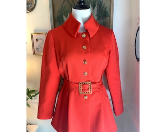 May include: A red, collared jacket with a gold buckle belt and gold buttons. The jacket has a slightly flared hem and long sleeves.