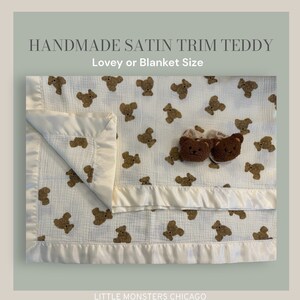 May include: A white muslin baby blanket with a satin trim and a brown teddy bear print. The blanket is folded in half and has a pair of brown teddy bear slippers on top. The text "HANDMADE SATIN TRIM TEDDY" and "Lovey or Blanket Size" is at the top of the image. The text "LITTLE MONSTERS CHICAGO" and "Teddy Collection" is at the bottom of the image.