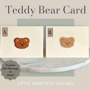 May include: Two blank greeting cards with a teddy bear embroidered on each. The card on the left has a brown teddy bear and the card on the right has a beige teddy bear. The cards are on a white marble surface. The text "Teddy Bear Card" is at the top of the image. The text "A." is in the top left corner of the card on the left. The text "B." is in the top left corner of the card on the right. The text "Custom Gift Message Or Blank" is in a circle in the bottom left corner of the image. The text "LITTLE MONSTERS CHICAGO" is at the bottom of the image.