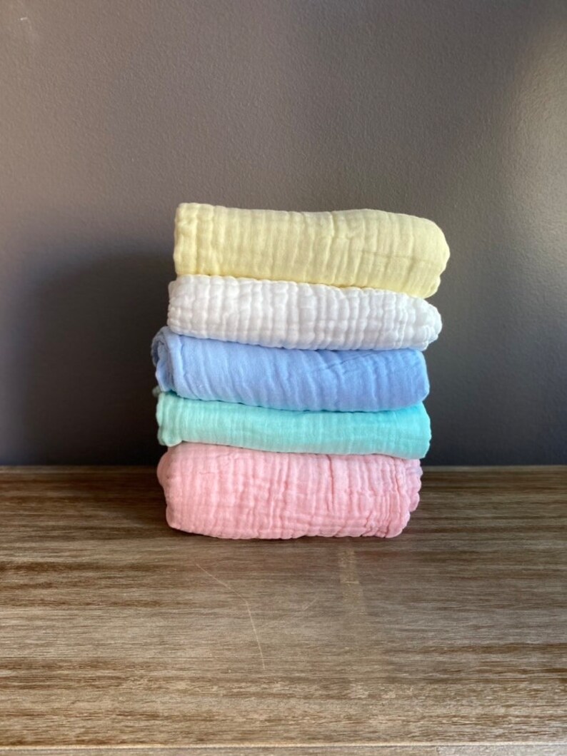 May include: A stack of five soft, textured baby blankets in pastel colours: yellow, white, light blue, mint green, and pink.