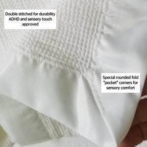 Op de afbeelding: Close-up van witte stof met een getextureerd oppervlak en gladde delen. De stof heeft dubbele stiksels voor duurzaamheid en afgeronde "pocket" hoeken voor sensorisch comfort. Tekst op de afbeelding luidt "ADHD and sensory touch approved."