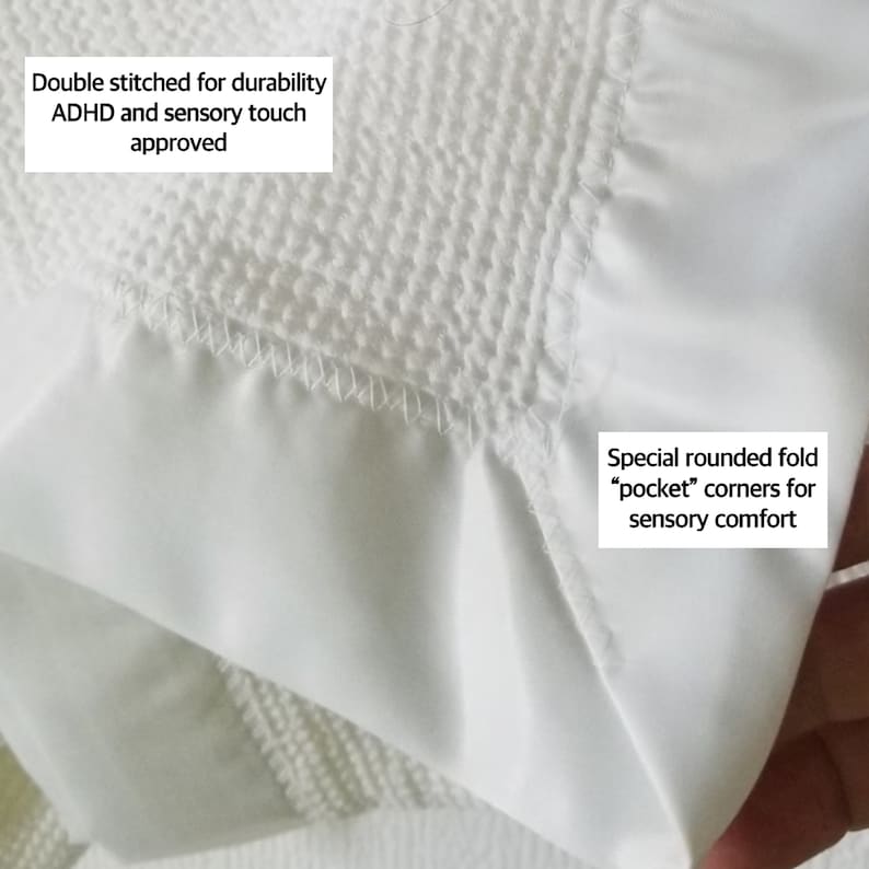 Op de afbeelding: Close-up van witte stof met een getextureerd oppervlak en gladde delen. De stof heeft dubbele stiksels voor duurzaamheid en afgeronde "pocket" hoeken voor sensorisch comfort. Tekst op de afbeelding luidt "ADHD and sensory touch approved."