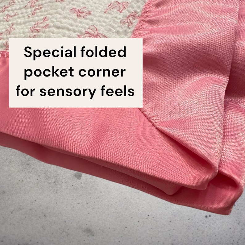 May include: Close-up of a pink fabric with a special folded pocket corner. The fabric has a satin-like texture and is a soft, light pink color. The text on the image reads: "Special folded pocket corner for sensory feels."