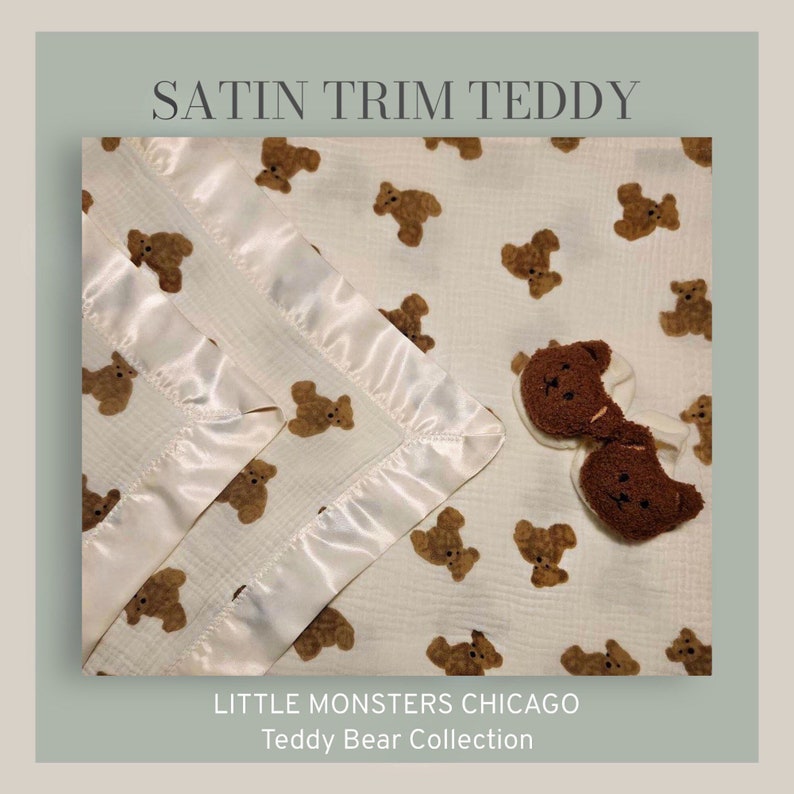 May include: A white muslin baby blanket with a satin trim and a brown teddy bear print. The blanket is folded in half and has a small brown teddy bear attached to it. The text "LITTLE MONSTERS CHICAGO Teddy Bear Collection" is printed on the blanket.