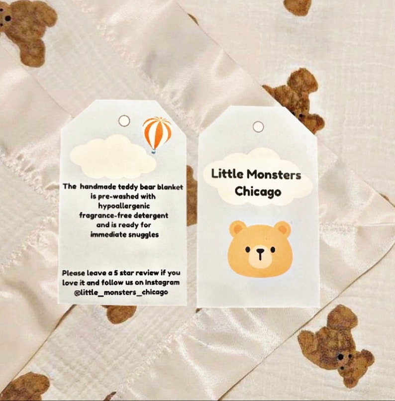 May include: Two white tags with rounded corners and a hole at the top. The tag on the left has a cartoon cloud with a hot air balloon and text that reads: "The handmade teddy bear blanket is pre-washed with hypoallergenic fragrance-free detergent and is ready for immediate snuggles. Please leave a 5 star review if you love it and follow us on Instagram @little_monsters_chicago". The tag on the right has a cartoon bear head and text that reads: "Little Monsters Chicago".