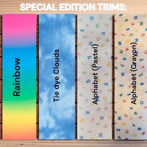 Op de afbeelding: Vier speciale editie trimontwerpen. De eerste is een regenboogverloop, gevolgd door een tie-dye wolkenpatroon. De derde en vierde ontwerpen hebben alfabetpatronen in pastel- en krijtkleuren. De tekst "SPECIAL EDITION TRIMS" staat bovenaan.