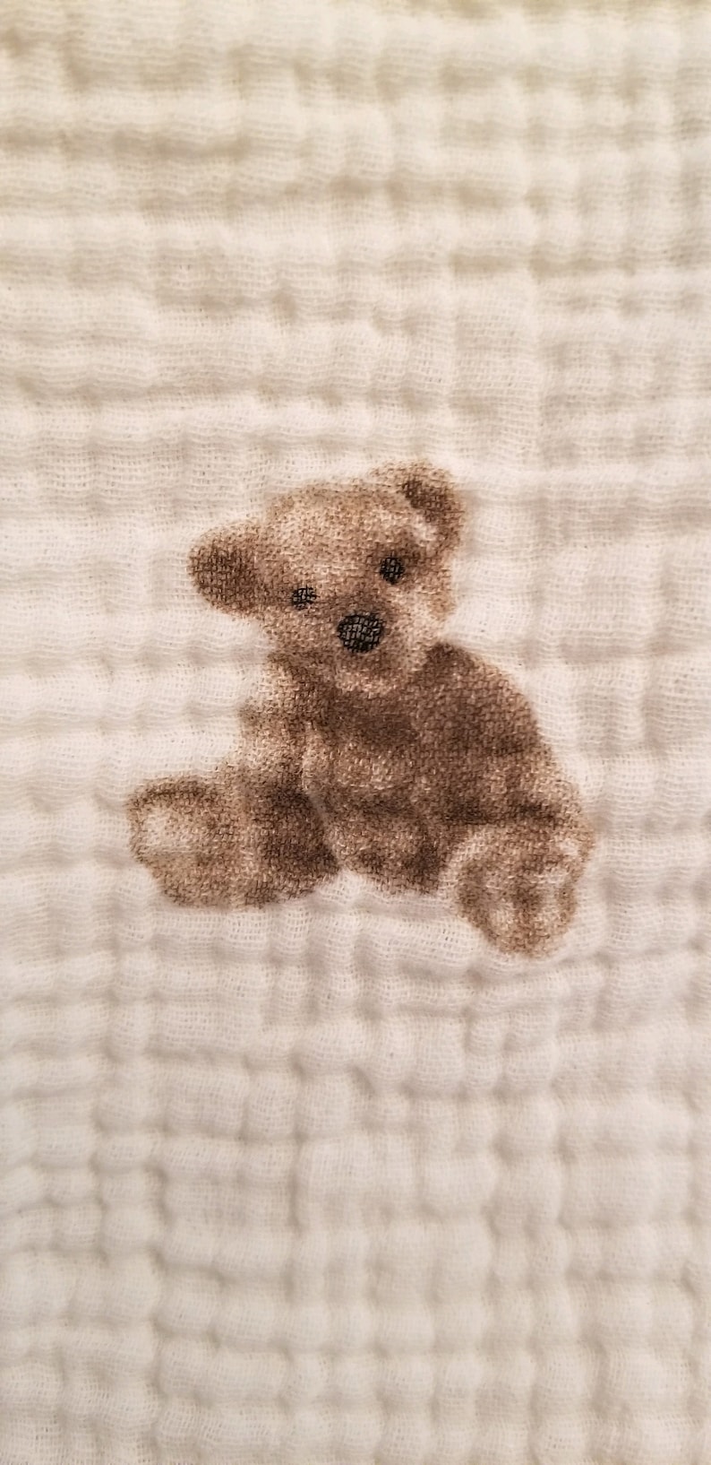 May include: A white muslin baby blanket with a brown teddy bear printed on it.