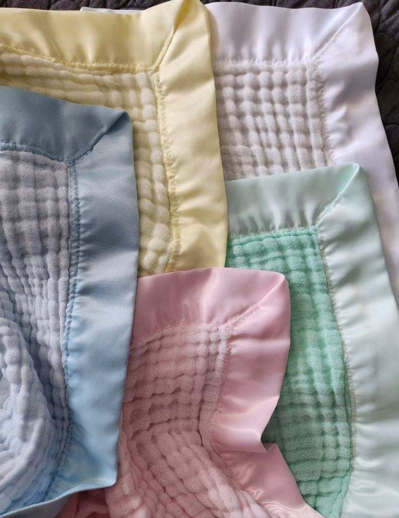 May include: Four baby blankets with satin trim. The blankets are in shades of yellow, white, pink, and green.
