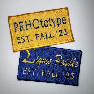 May include: Two embroidered patches, one yellow and one blue, with the text "PRHOtotype EST. FALL '23" and "Sigma Poodle EST. FALL '23".