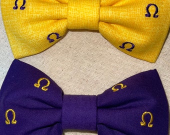 Può includere: Due papillon, uno giallo e uno viola, con simboli omega ricamati in oro.