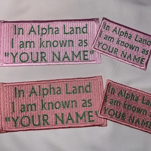 May include: Four pink and green embroidered patches with the text "In Alpha Land I am known as "YOUR NAME""