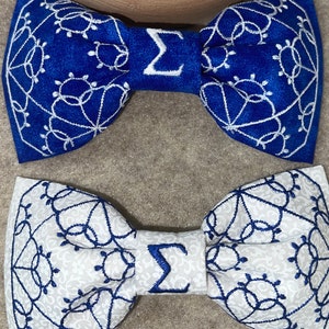 May include: Two bow ties, one blue with white embroidery and one white with blue embroidery. Both have a white embroidered Greek letter sigma in the center.