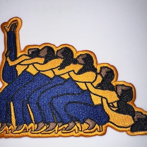 May include: Embroidered patch featuring a stylized design of figures in blue pants and yellow tops, with black hair. The patch has a gold border. The figures appear to be in motion, possibly dancing or interacting.