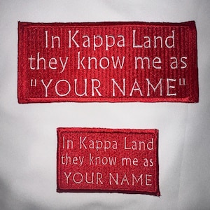 May include: Two red rectangular patches with white embroidered text. The larger patch reads "In Kappa Land they know me as "YOUR NAME"". The smaller patch reads "In Kappa Land they know me as YOUR NAME".