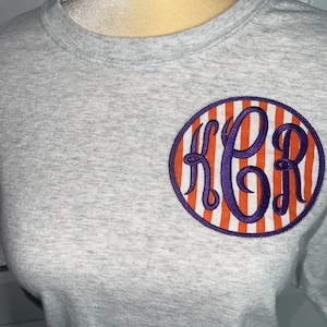 May include: A gray t-shirt with a purple and orange striped circle with the letters "FPR" in purple inside the circle.