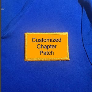 May include: A blue shirt with a rectangular, orange patch. The patch has gold stitching around the edges and the words "Customized Chapter Patch" in dark blue text.