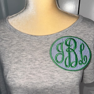May include: Gray t-shirt with a green and blue monogrammed patch on the front.