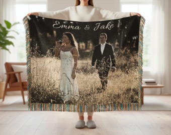 May include: A personalized woven throw blanket featuring a sepia-toned wedding photo of a couple in a field. The blanket has a fringed edge with teal, brown, and orange threads. The names "Emma & Jake" are written in script.