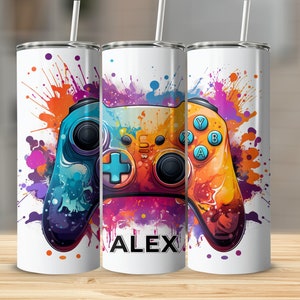 Puede incluir: Un vaso de acero inoxidable blanco con un diseño de salpicaduras de pintura de colores que presenta un mando de videojuego. El texto "ALEX" está impreso en el vaso.
