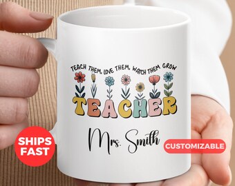 Op de afbeelding: Een witte keramische mok met een kleurrijk bloemenontwerp en de tekst "TEACH THEM, LOVE THEM, WATCH THEM GROW TEACHER Mrs. Smith CUSTOMIZABLE".