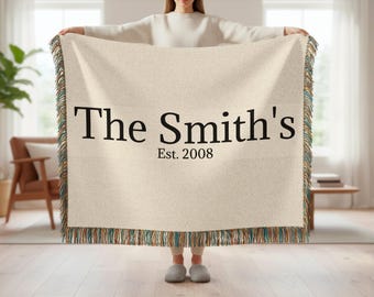 May include: Cream-colored woven throw blanket with fringed edges in shades of teal, brown, and tan. The text "The Smith's" and "Est. 2008" are printed in black across the center of the blanket.