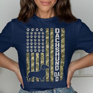 Dark blue t-shirt with camouflage flag and dachshund silhouette, reads "DACHSHUND DAD".
