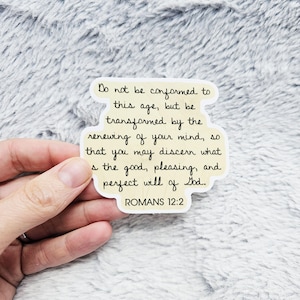 May include: A sticker with a light yellow background and black text. The text reads: "Do not be conformed to this age, but be transformed by the renewing of your mind, so that you may discern what is the good, pleasing, and perfect will of God. ROMANS 12:2."