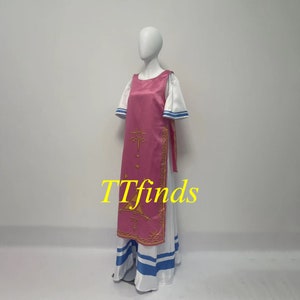 Pode incluir: Um vestido rosa e branco com um design dourado. O vestido tem uma saia longa com listras azuis e um corpete rosa com um design dourado. O vestido est&aacute; em um manequim branco.