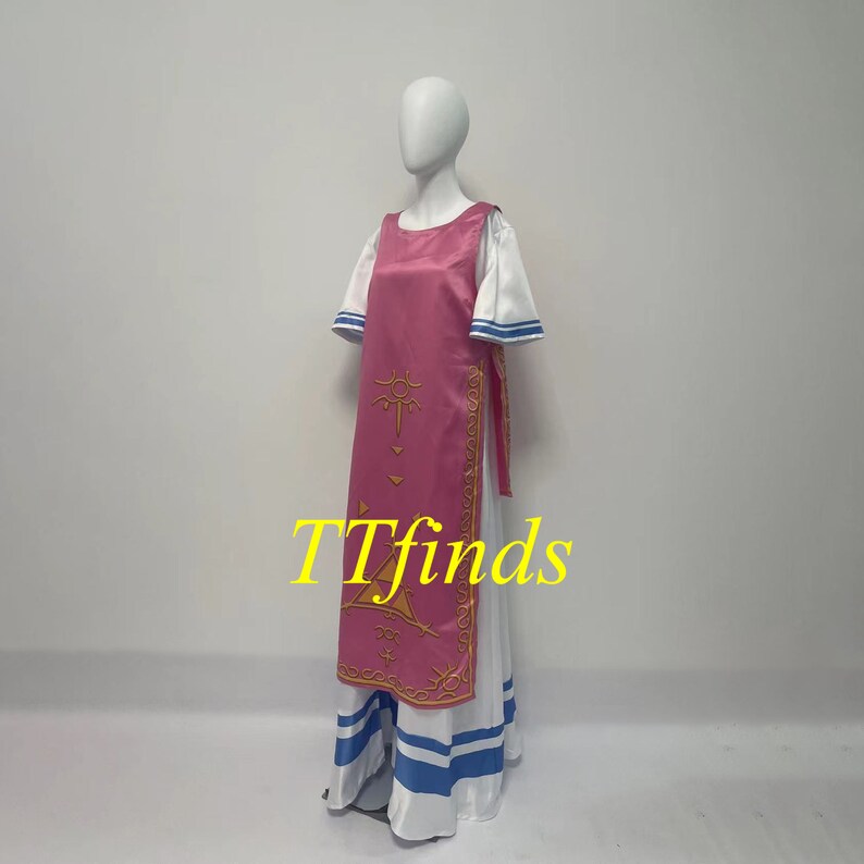 Pode incluir: Um vestido rosa e branco com um design dourado. O vestido tem uma saia longa com listras azuis e um corpete rosa com um design dourado. O vestido est&aacute; em um manequim branco.