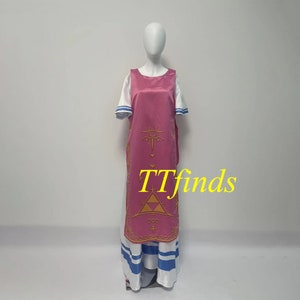 Pode incluir: Um vestido rosa e branco com um design dourado. O design apresenta um tri&acirc;ngulo com um c&iacute;rculo dentro e um s&iacute;mbolo acima. O vestido tem uma camiseta branca com listras azuis na parte inferior.