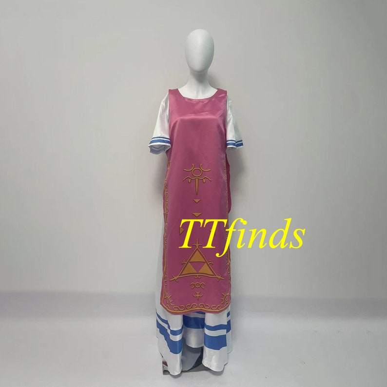 Pode incluir: Um vestido rosa e branco com um design dourado. O design apresenta um tri&acirc;ngulo com um c&iacute;rculo dentro e um s&iacute;mbolo acima. O vestido tem uma camiseta branca com listras azuis na parte inferior.