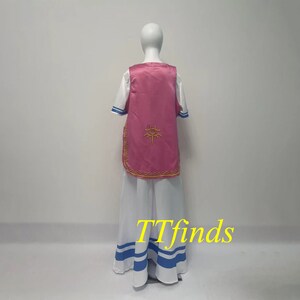 Pode incluir: Um traje rosa e branco com um s&iacute;mbolo dourado nas costas. O traje inclui uma saia longa com listras azuis, uma camisa branca com detalhes azuis e um colete rosa.