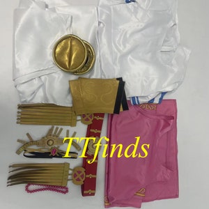 Pode incluir: Um conjunto de fantasia de cosplay que inclui uma blusa branca com detalhes azuis, uma blusa rosa, um cinto dourado, um chap&eacute;u dourado e um colar dourado e rosa.