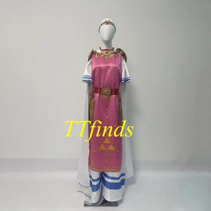 Pode incluir: Um vestido rosa e branco com detalhes dourados e um design triangular na frente. O vestido tem uma capa branca e listras azuis e brancas na parte inferior.