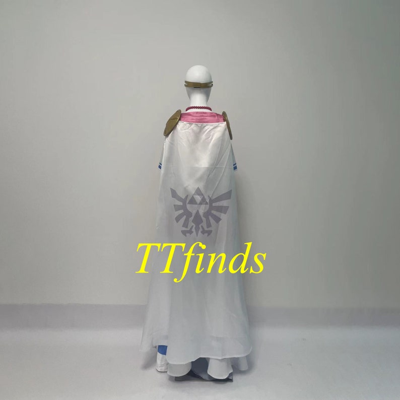 Pode incluir: Fantasia de cosplay branca com detalhes azuis e dourados. A fantasia inclui uma capa longa com um grande s&iacute;mbolo Triforce cinza nas costas. O texto "TTfinds" est&aacute; impresso em amarelo na capa.