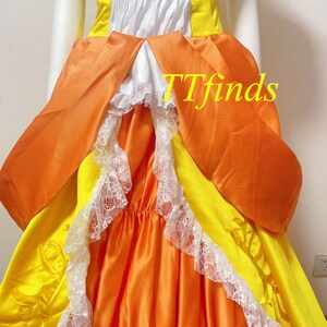 May include: A yellow and orange dress with white lace trim and a white bodice. The dress has a large bow in the back and is made of a satin-like fabric. The dress is a vintage style and is perfect for a special occasion.